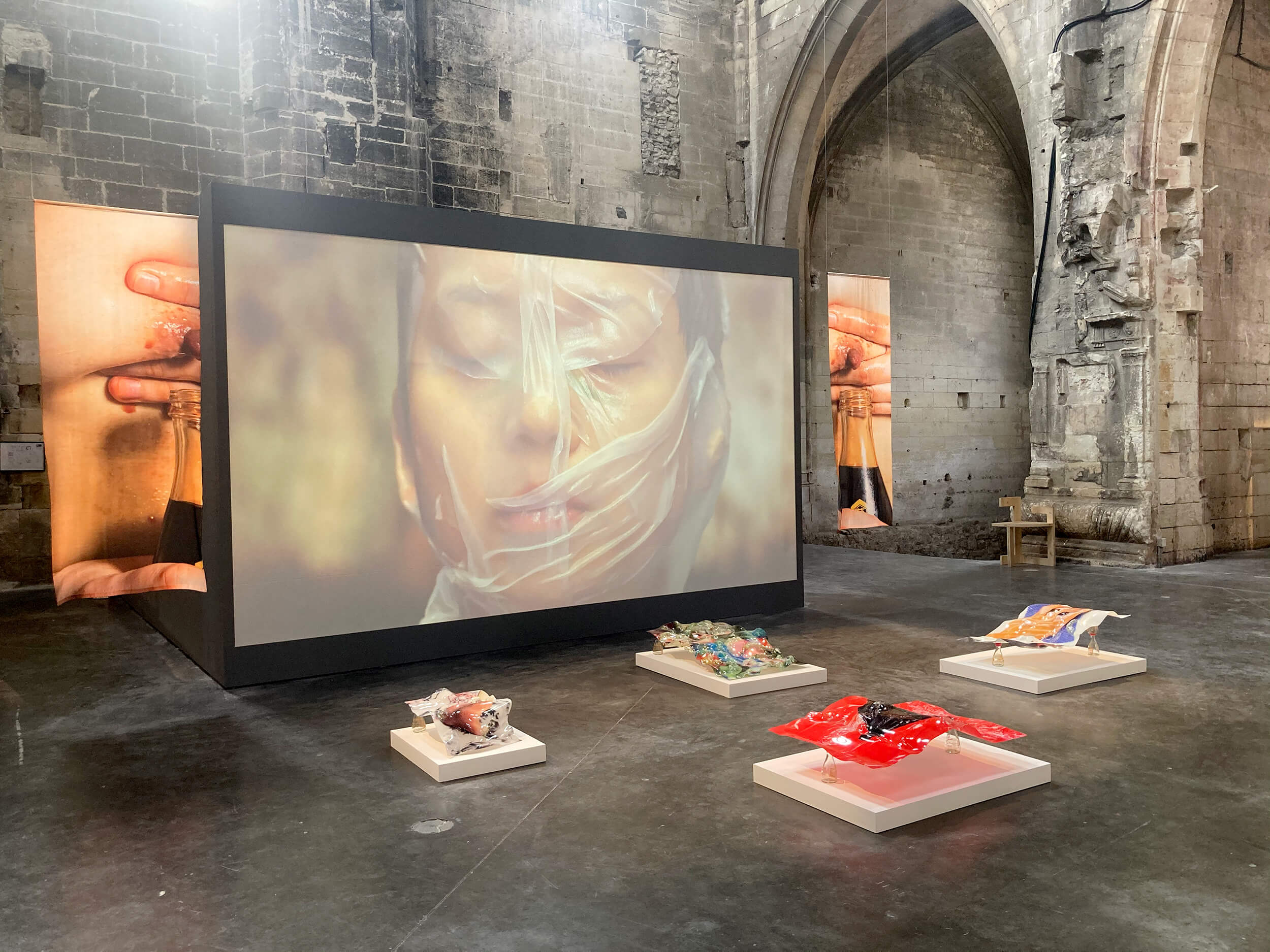 Installation 'Across the Ocean' by Hiền Hoàng at the Louise Roederer Discovery Award 2023, Rencontres de la Photographie d'Arles 2023. The installation features bended UV printed plexiglass from the 'Asia Bistro' series, postcards, thermal printed textiles, and a performance video of 'Made in Rice.' Explores clichés and traumatic immigrant experiences, inspired by the artist's late aunt's journey in the GDR and personal reflections."