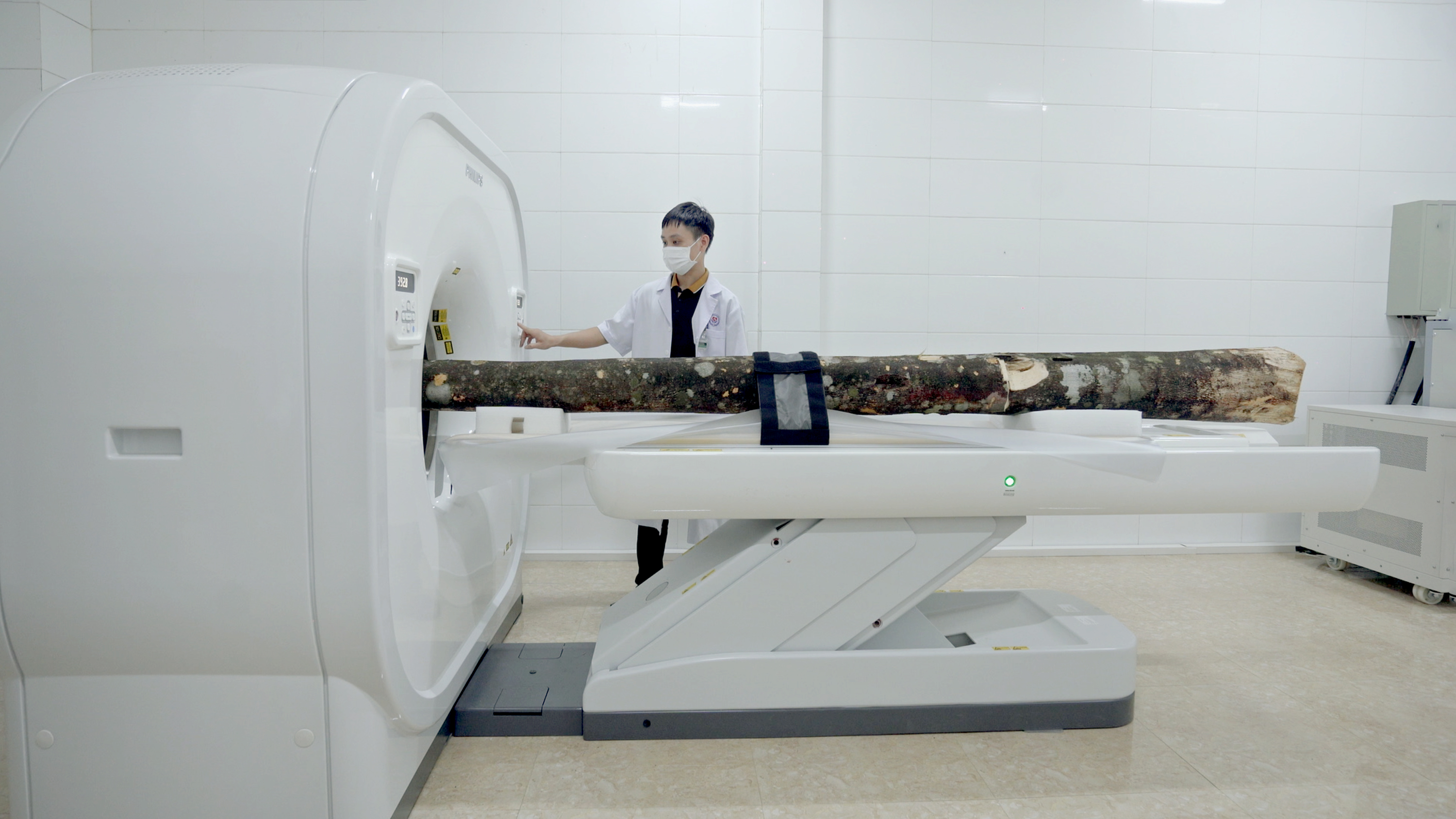 Still from the documentation video from „Scent from Heaven“. The artist is conducting an experiment with a CT Scanner and an Aquilaria tree. The CT Scan should show the inner structure of the tree, which then could reveal the Agarwood inside the tree, as well as the images of the pain the tree has been enduring. The experiment was taken place in Huong Khe Clinics, Ha Tinh, Vietnam.
